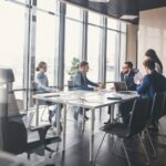 people sitting at a conference room table with windows in background_s