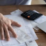 On desk lot of receipts, calculator and laptop